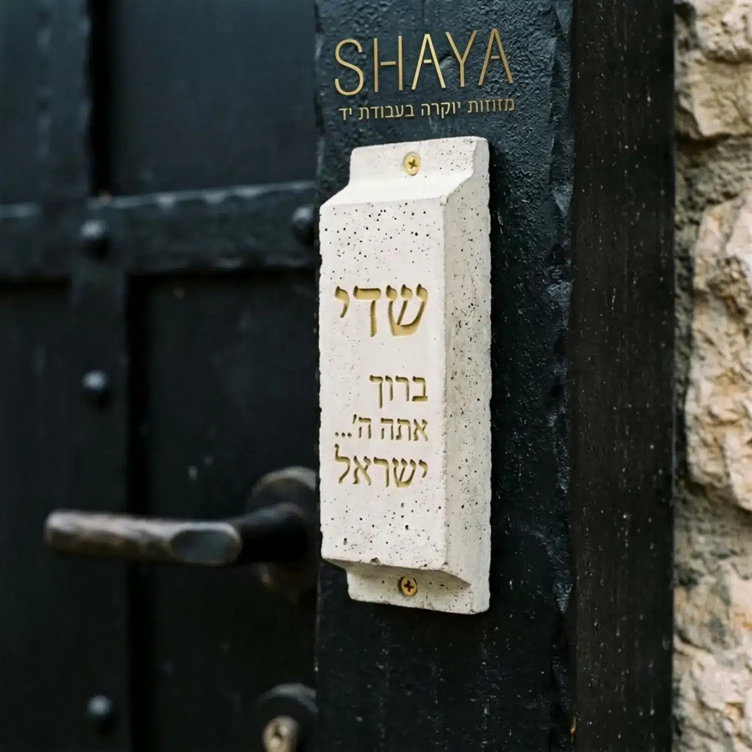 תמונה תקריב של מזוזה מעוצבת מבטון המותקנת על משקוף דלת כניסה מרשימה מפלדה שחורה, הממחישה ניגודיות חומרים וטקסטורות מודרניות